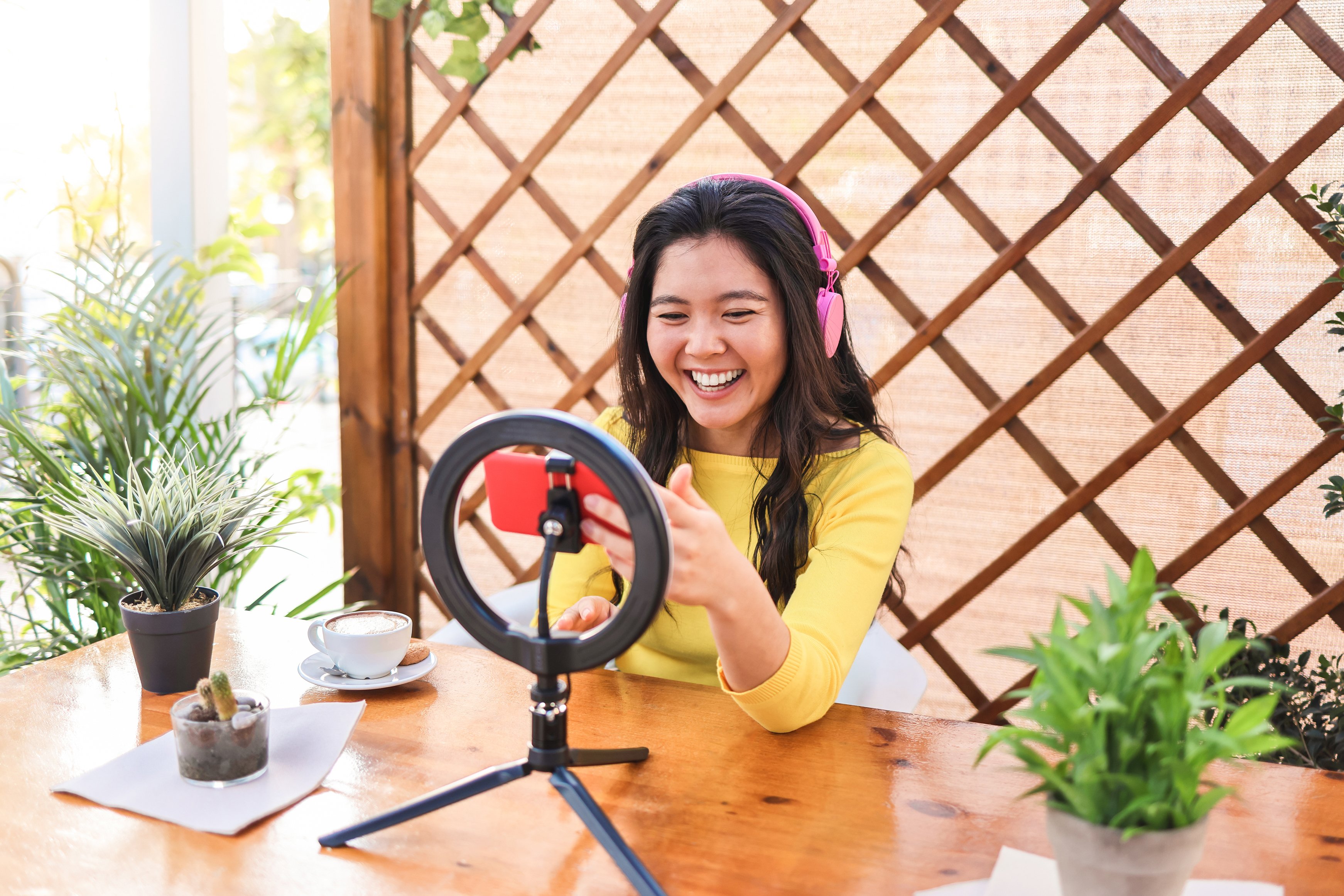 An Asian influencer streaming online with her smartphone outdoors at a restaurant for social media marketing.