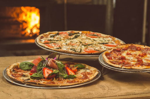 Three delicious pizzas are served in front of a fireplace ready for eating.