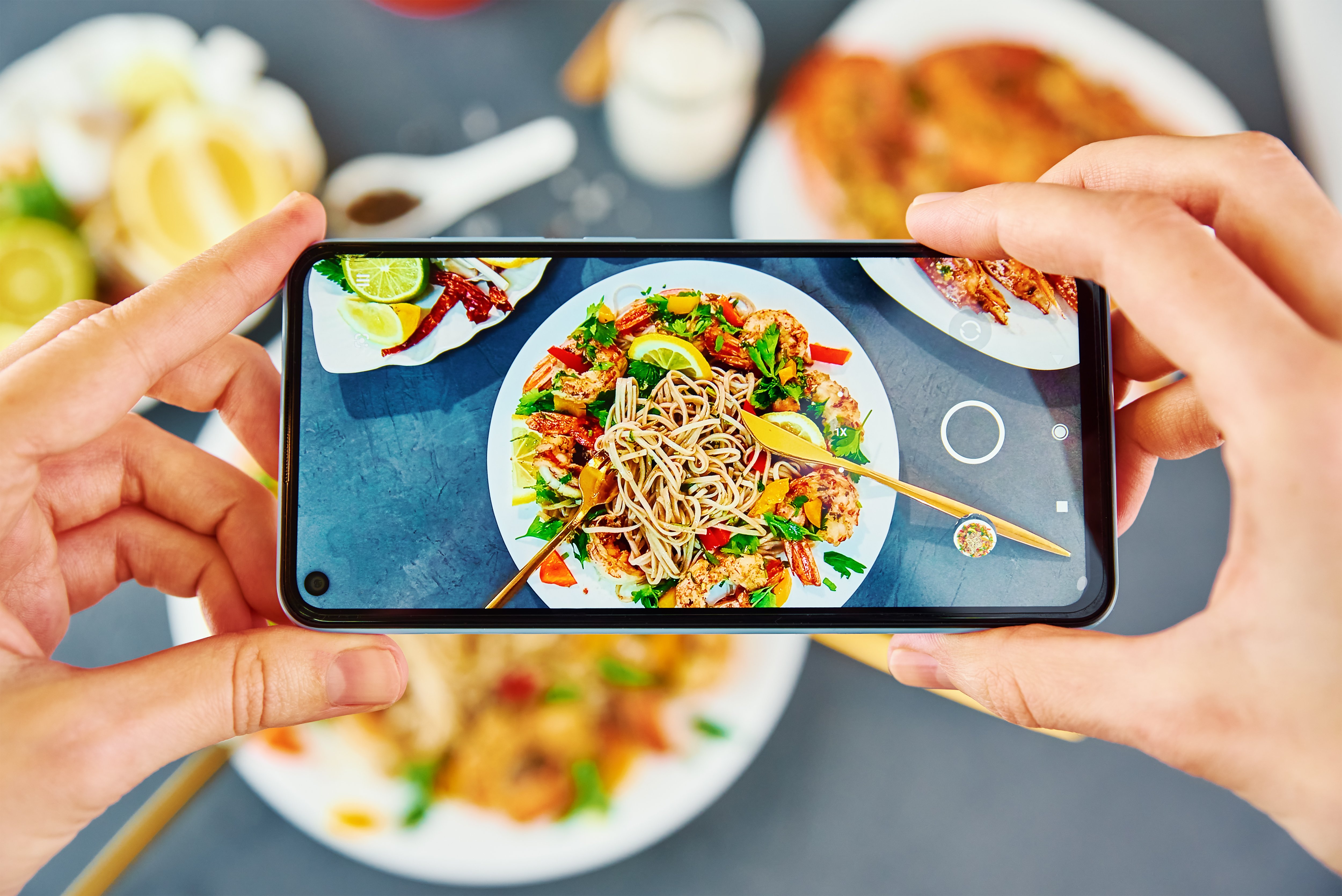 An individual taking a photo of stir fry noodles with a smartphone for restaurant social media marketing.
